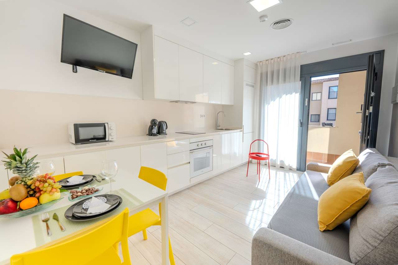 Salón con cocina equipada, mesa de comedor y sofá cama en un apartamento de un dormitorio