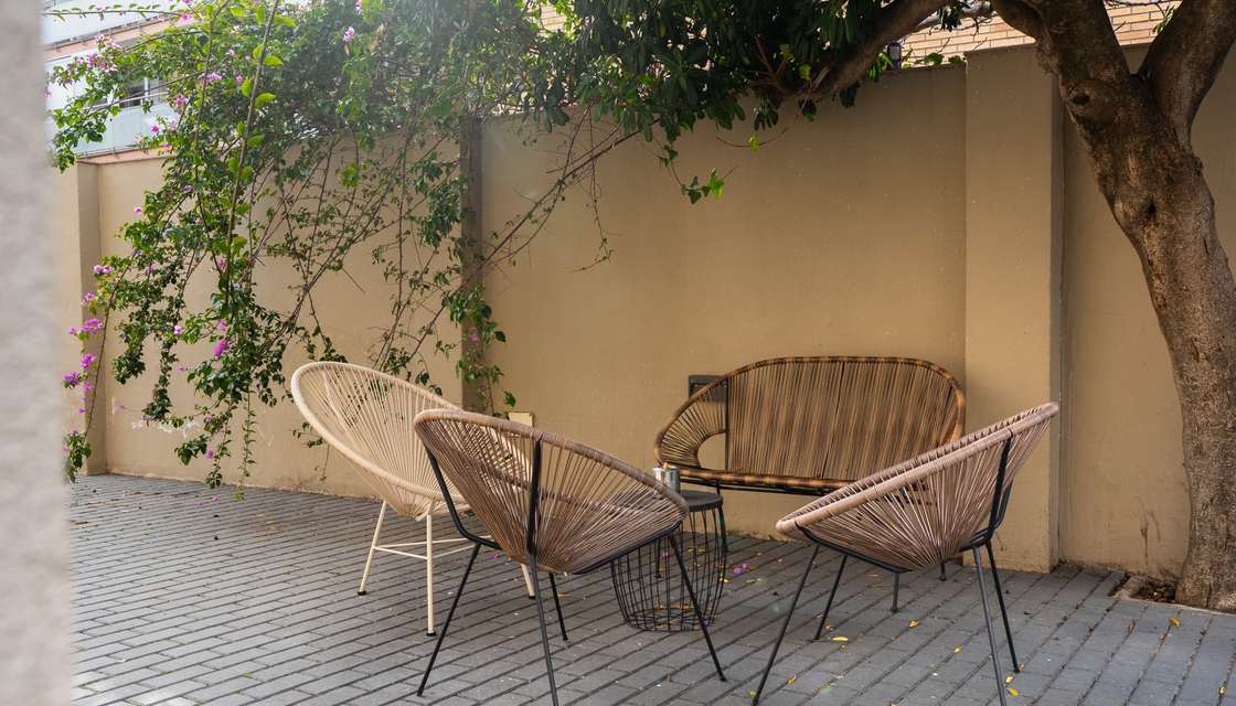Rincón del patio con sillas de mimbre a la sombra de un árbol