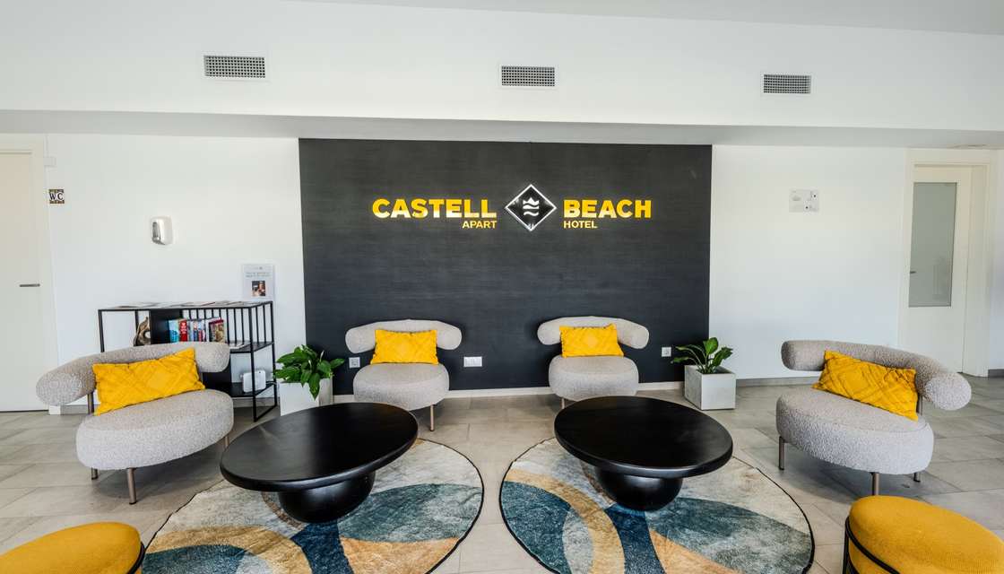 Recepción de Castell Beach Aparthotel con el logotipo en la pared y butacas con cojines amarillos