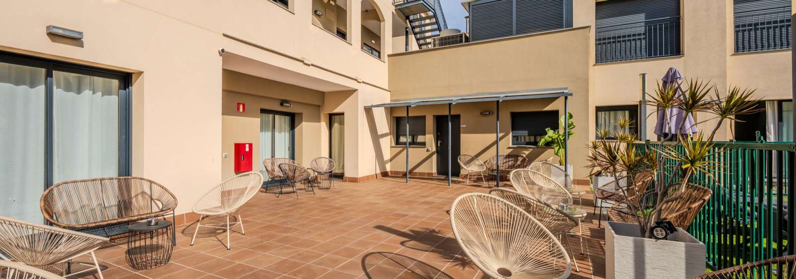 Patio interior del Castell Beach Aparthotel en Castelldefels, con sillas de rejilla y los apartamentos alrededor