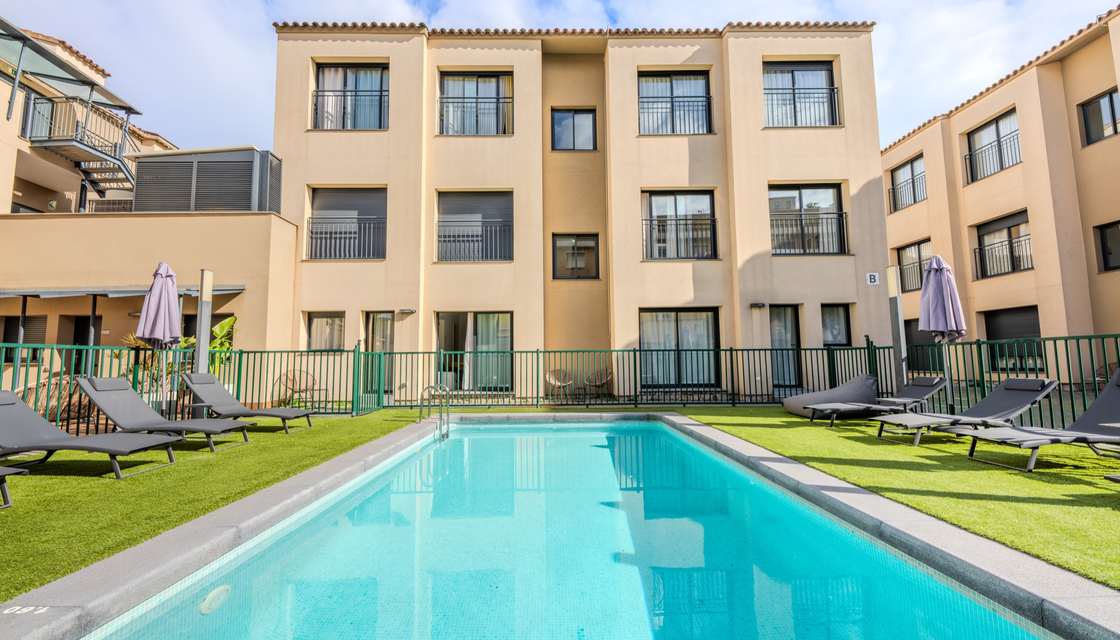 Piscina exterior con tumbonas y el edificio de apartamentos al fondo