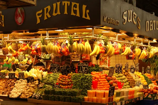 Un puesto de fruta de la Boqueria, lleno de plátanos, piñas y fruta de colores