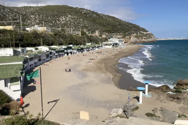 La playa de Garraf con sus casetas blancas y verdes, al pie de las montañas del Garraf que bajan al mar