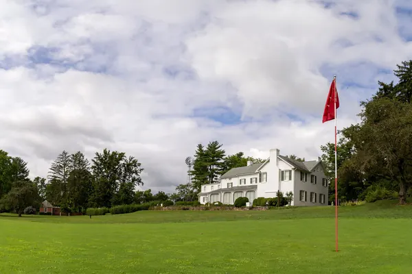 Un green de golf con su bandera roja junto a una casa blanca (foto genérica, no es el Club de Golf Terramar)