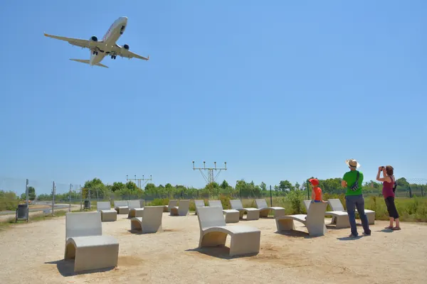 Un avión pasa muy bajo sobre el mirador de El Prat, con sus bancos de piedra junto a las luces de aproximación