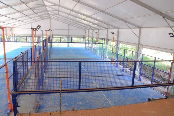 Una pista de pádel cubierta y vacía, con el suelo azul y las paredes de cristal (foto genérica, no es Padelarium)
