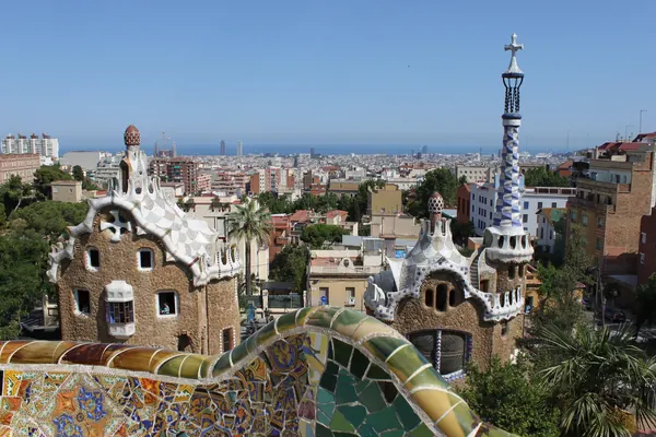 Las casetas de la entrada del Park Güell y el banco de trencadís, con Barcelona y el mar al fondo