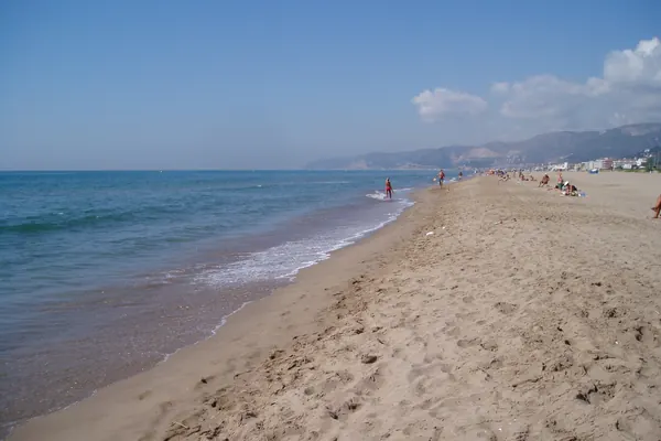 Playa de Castelldefels de arena dorada junto al mar, con las montañas del Garraf al fondo