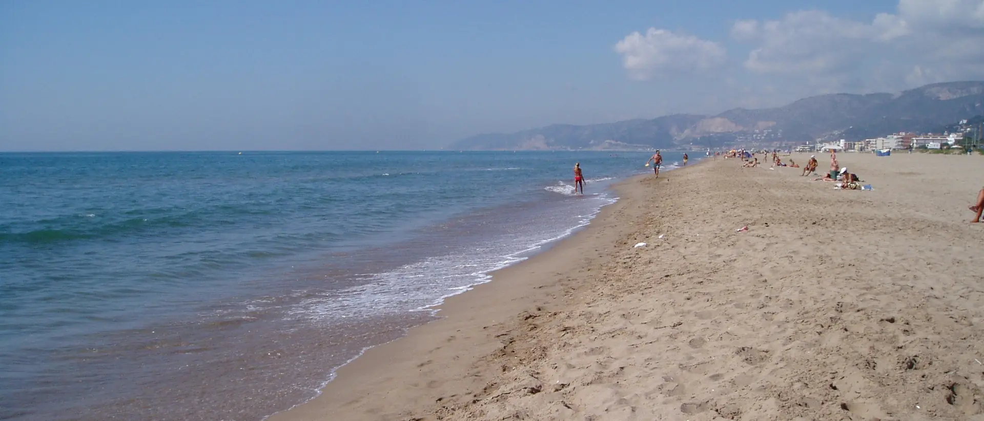 Playa de Castelldefels de arena dorada junto al mar, con las montañas del Garraf al fondo