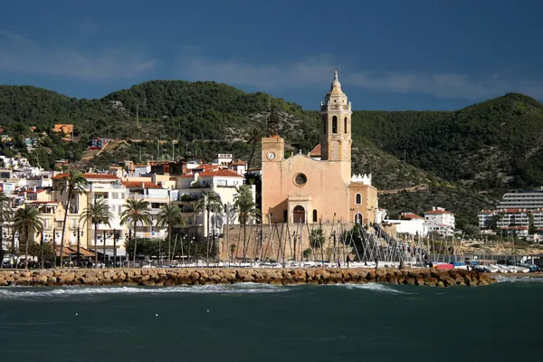 Sitges desde el mar: la iglesia de Sant Bartomeu i Santa Tecla sobre el paseo, con las casas blancas y las colinas detrás