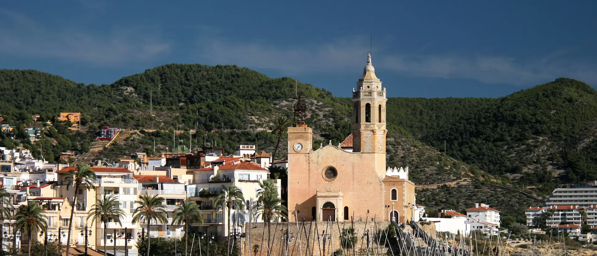 Sitges desde el mar: la iglesia de Sant Bartomeu i Santa Tecla sobre el paseo, con las casas blancas y las colinas detrás